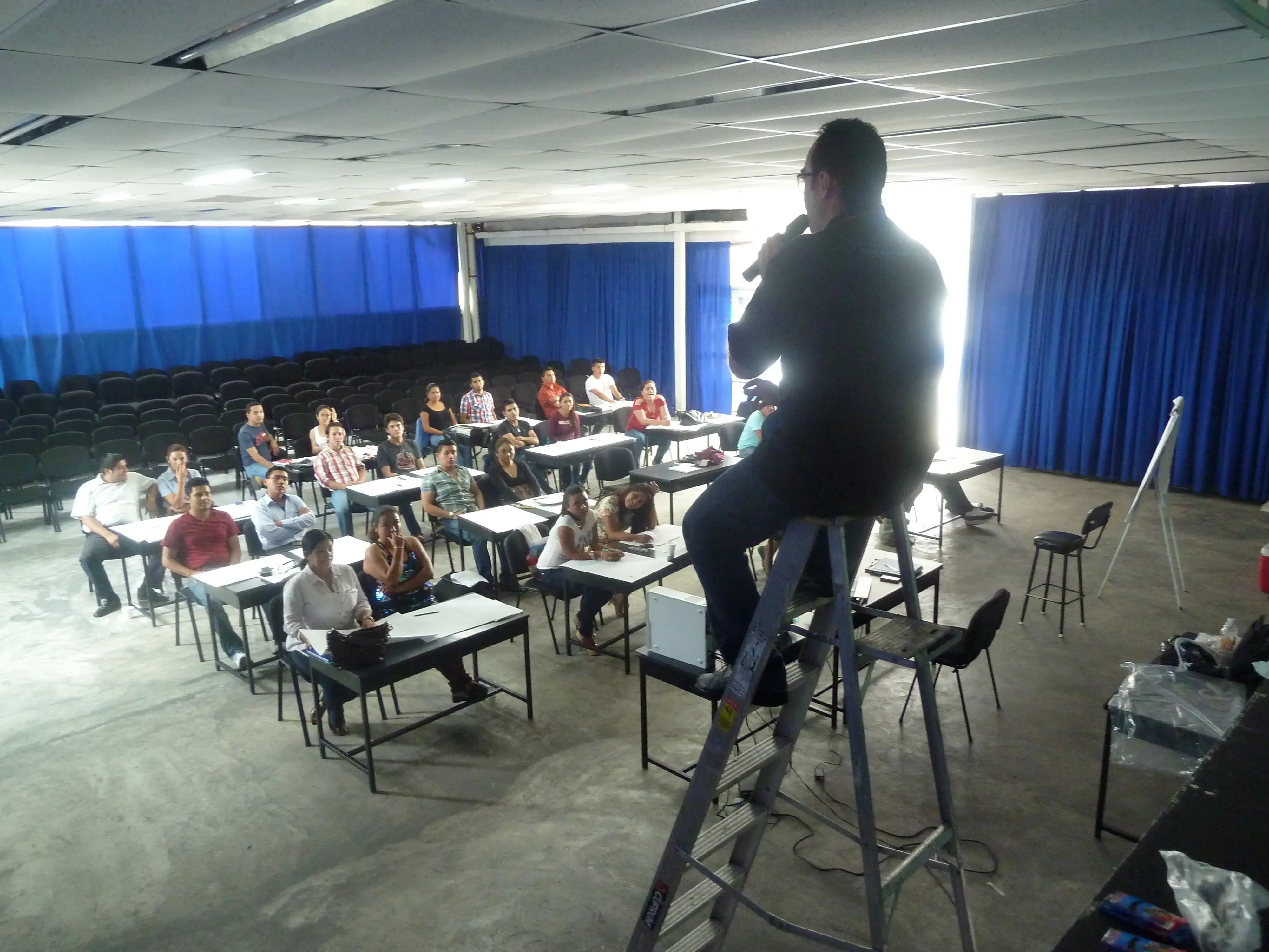 Coach motivacional subido a una escalera mientras imparte sesión interactiva en un centro de entrenamiento empresarial con ambiente participativo y enfocado. 