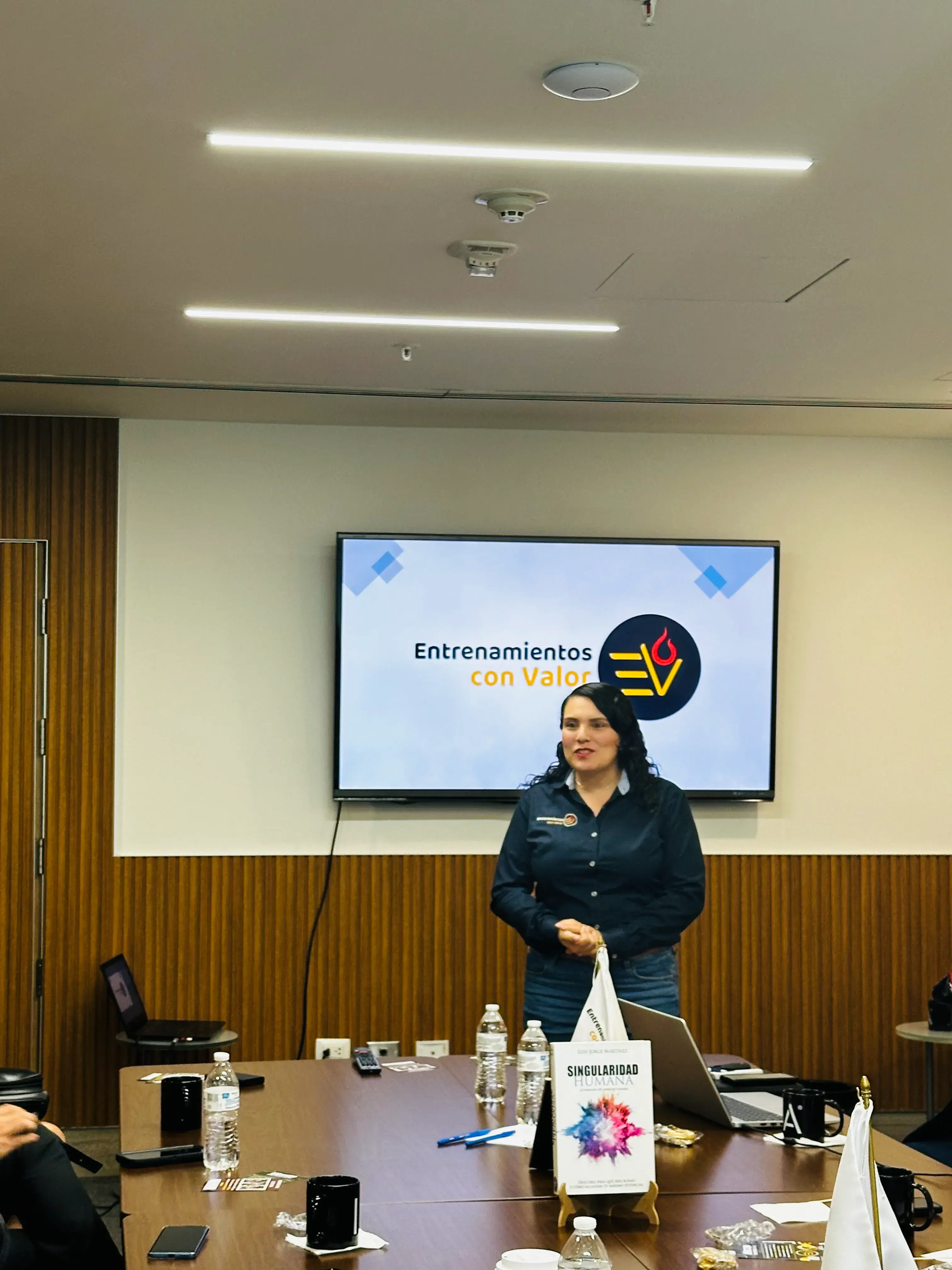 Mujer frente a una pantalla que dice entrenamientos con valor Mujer observando una pantalla que proyecta el mensaje “entrenamientos con valor”, parte de una sesión práctica de coaching empresarial para líderes de equipo.