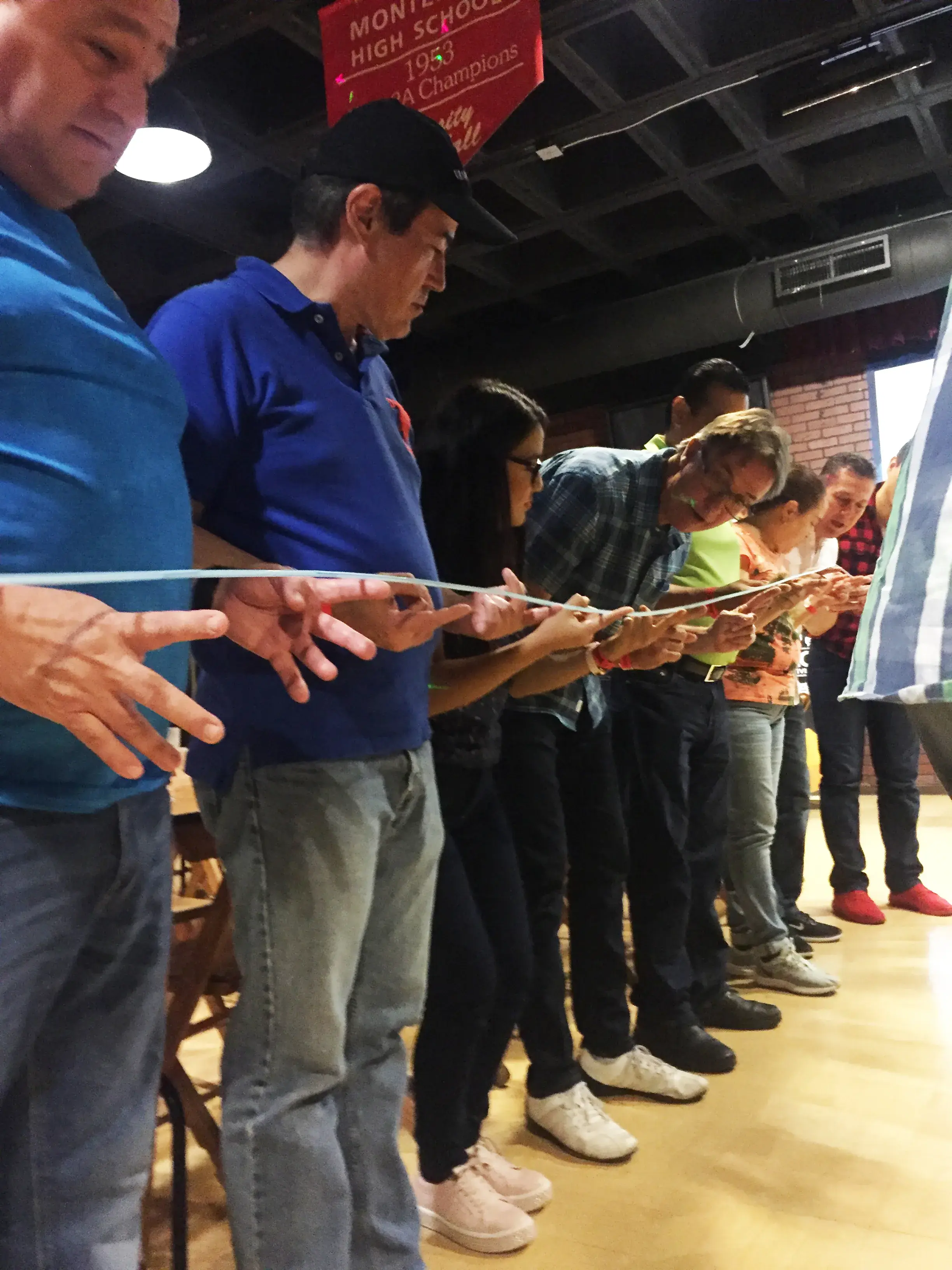 Team Building Monterrey: Unidos para el éxito En esta dinámica de team building Monterrey, un grupo de personas trabaja en conjunto para equilibrar y bajar una vara ligera usando solo sus dedos.