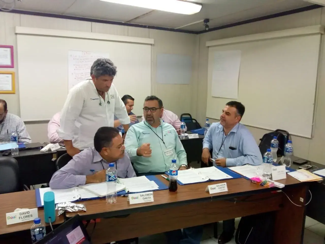 Coach se acerca a los empleados para resolver dudas en sesión de comunicación empresarial Coach empresarial interactúa con los empleados durante una sesión práctica para resolver dudas clave sobre comunicación empresarial dentro de equipos de trabajo.