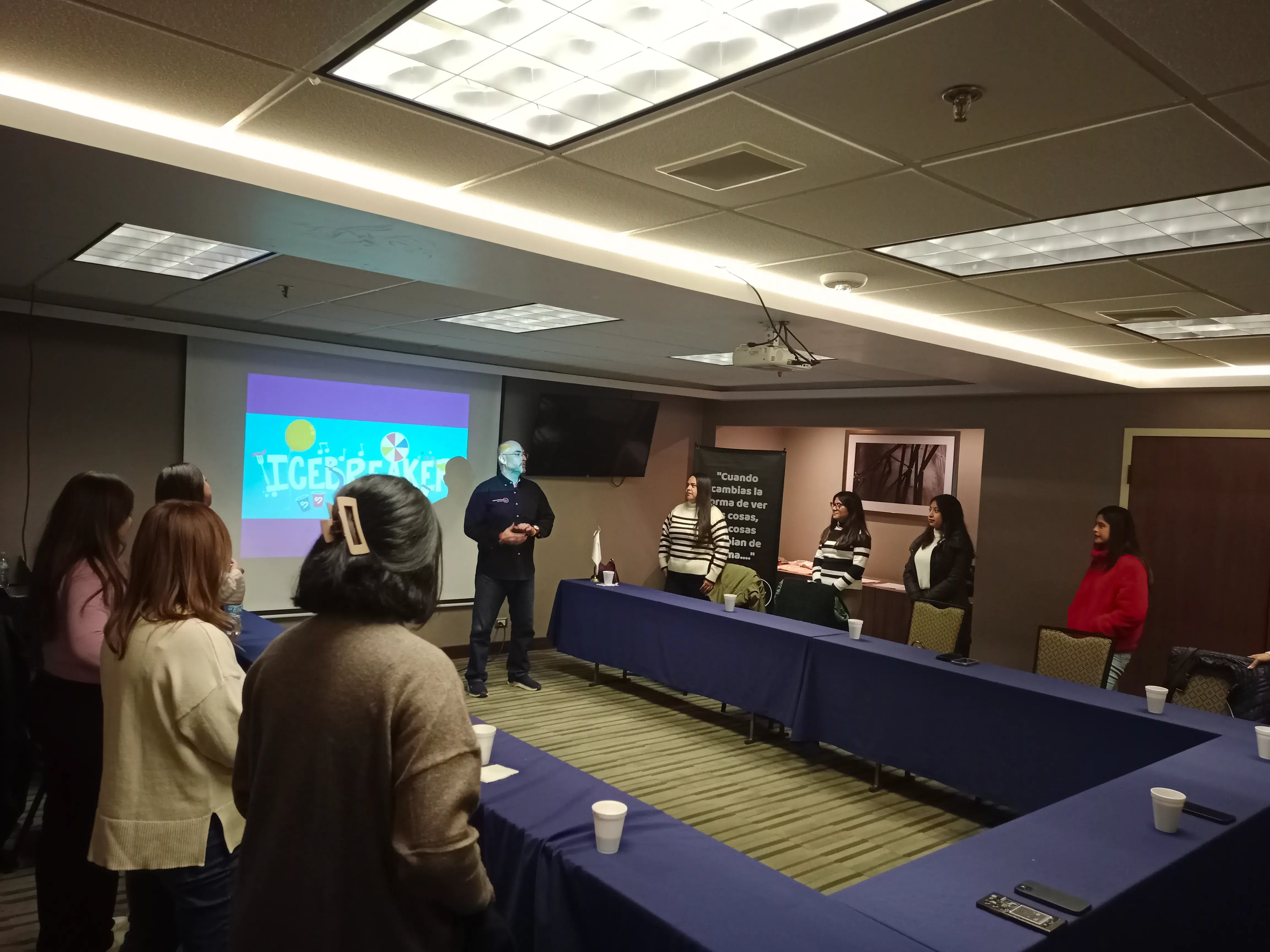 Hombre al centro de un salón exponiendo sobre comunicación empresarial Ponente al centro de un salón empresarial dirigiéndose a los asistentes, en una sesión de formación enfocada en fortalecer la comunicación empresarial efectiva.