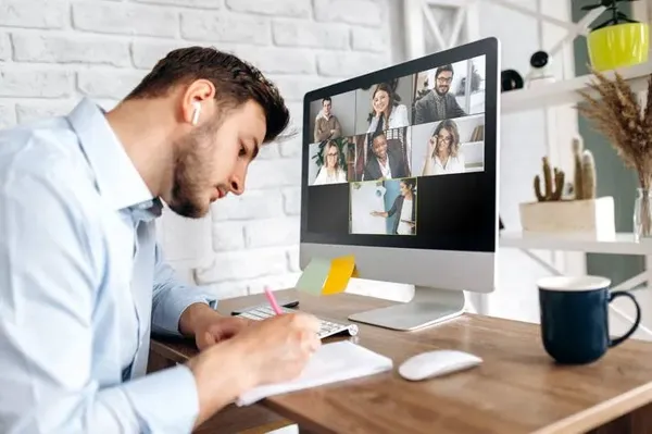 Cursos de Ventas Online - Mejora tus Habilidades Un hombre participa en una videollamada de un curso online, tomando notas. Esta imagen representa la dedicación a aprender y mejorar a través de nuestros cursos de ventas.
